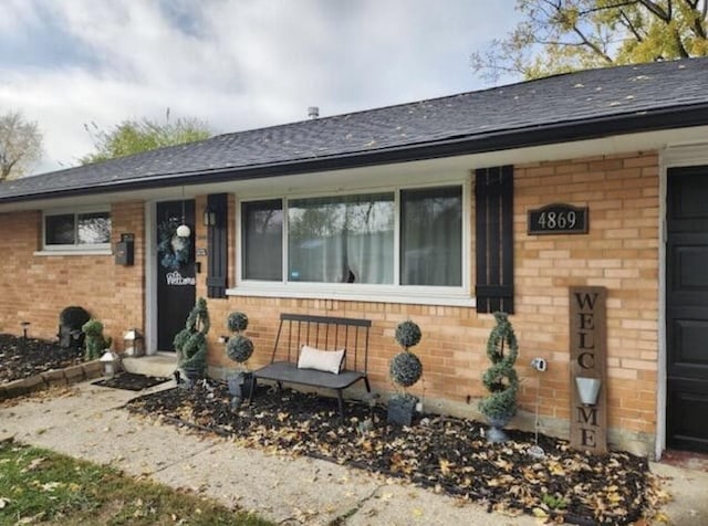 view of exterior entry featuring a garage, brick siding, and a shingled roof