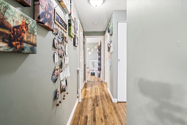 hallway featuring a textured ceiling, light wood-type flooring, and baseboards