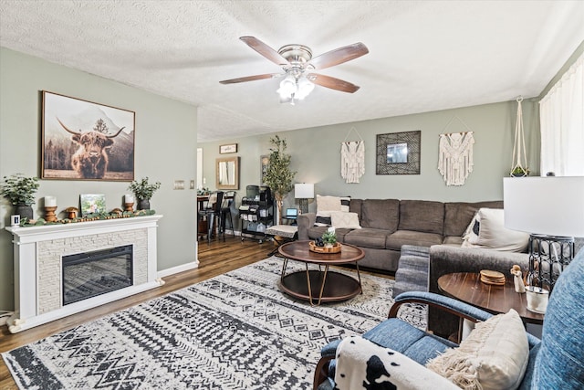 living area featuring a textured ceiling, ceiling fan, a fireplace, and wood finished floors