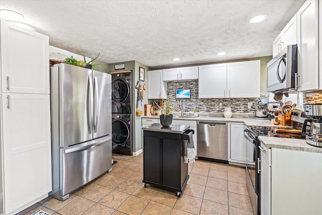 kitchen featuring backsplash, white cabinetry, stainless steel appliances, and stacked washer / dryer