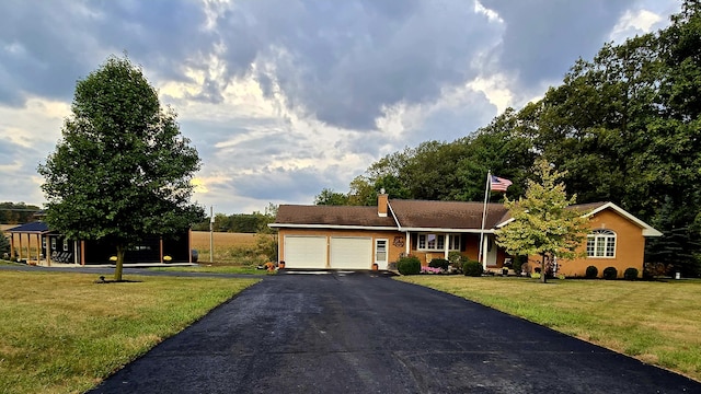 ranch-style home featuring a front lawn, a chimney, a garage, and aphalt driveway