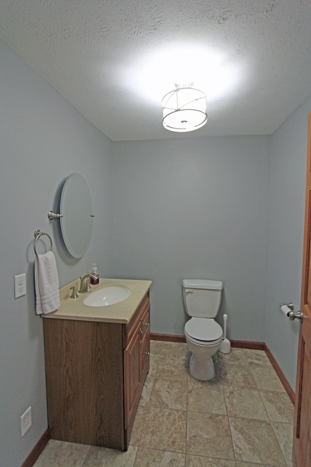 bathroom featuring baseboards, a textured ceiling, toilet, and vanity