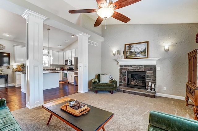 living area featuring baseboards, visible vents, lofted ceiling, decorative columns, and a stone fireplace