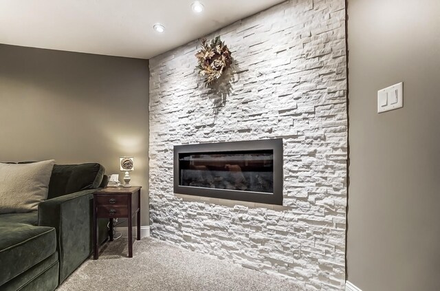 carpeted living area featuring a stone fireplace and baseboards