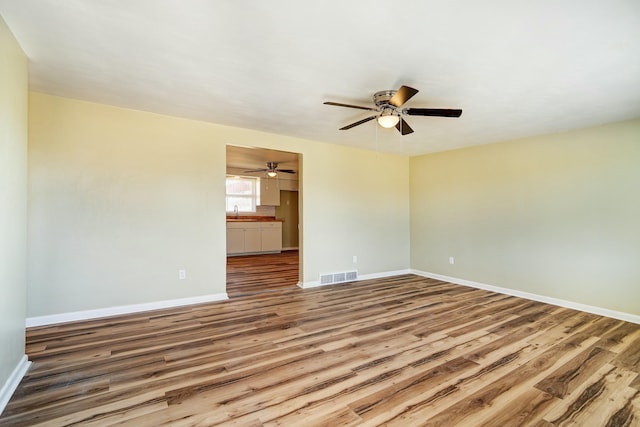 empty room featuring visible vents, baseboards, wood finished floors, a ceiling fan, and a sink