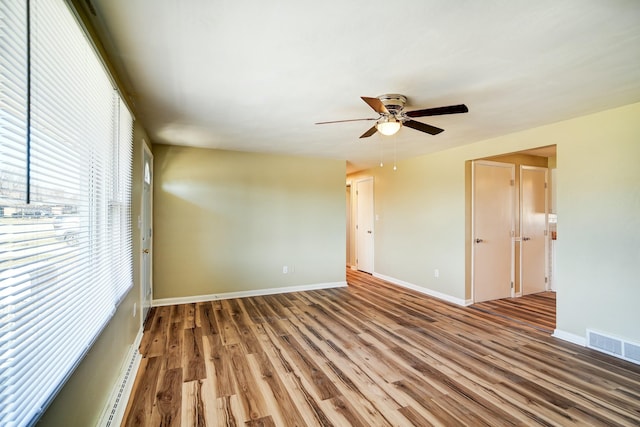 unfurnished room with wood finished floors, a ceiling fan, visible vents, and baseboards