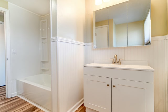 full bathroom featuring vanity, washtub / shower combination, wood finished floors, and wainscoting