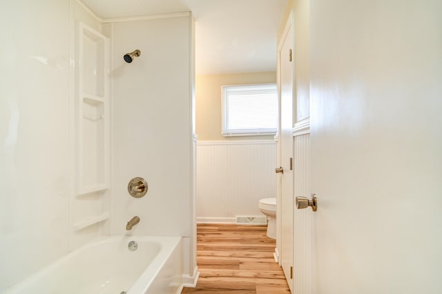 bathroom with wood finished floors, visible vents, wainscoting, shower / tub combination, and toilet