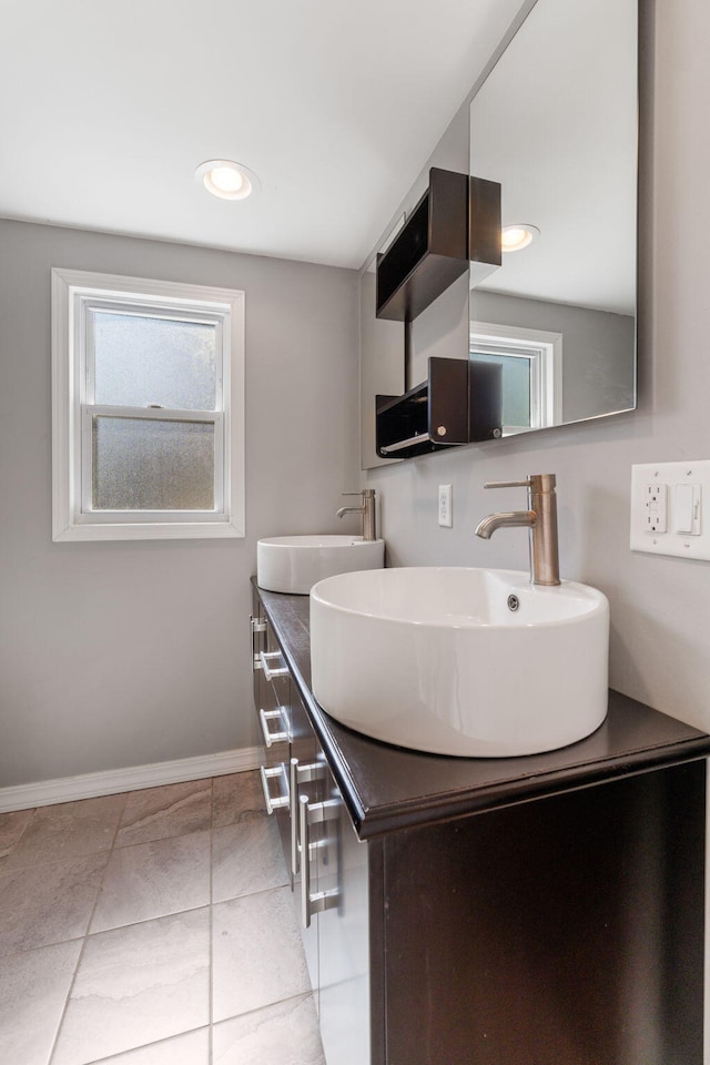 full bath with double vanity, tile patterned floors, baseboards, and a sink