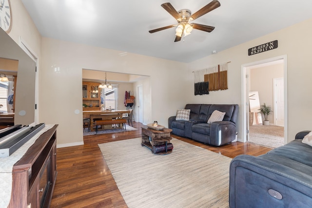 living room featuring ceiling fan with notable chandelier, dark wood-style floors, and baseboards