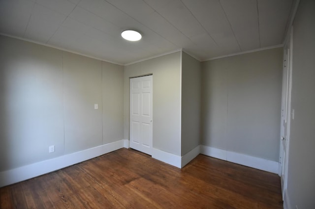 empty room featuring crown molding, dark wood-type flooring, and baseboards