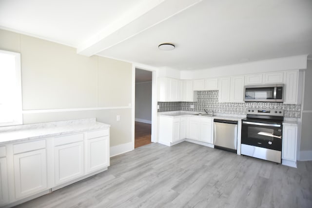 kitchen featuring backsplash, light wood-type flooring, appliances with stainless steel finishes, white cabinetry, and a sink