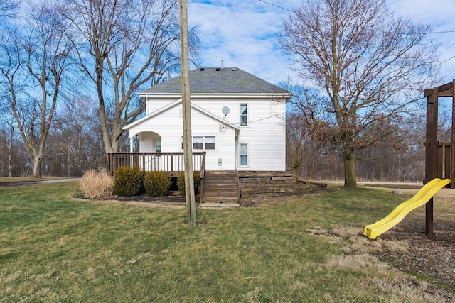 back of house with a wooden deck, a playground, and a lawn