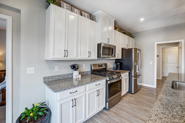 kitchen featuring sink, white cabinets, stainless steel appliances, light stone countertops, and light wood-type flooring