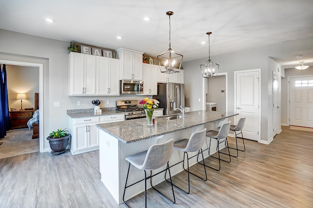 kitchen featuring appliances with stainless steel finishes, white cabinetry, a kitchen bar, light stone counters, and a center island with sink