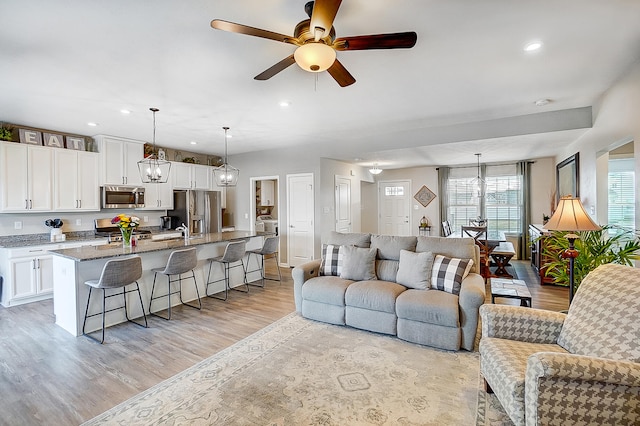 living room with ceiling fan with notable chandelier, sink, and light hardwood / wood-style floors