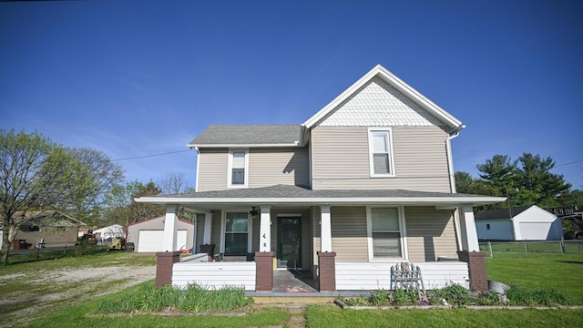 farmhouse inspired home with a porch, a front yard, dirt driveway, an outbuilding, and fence
