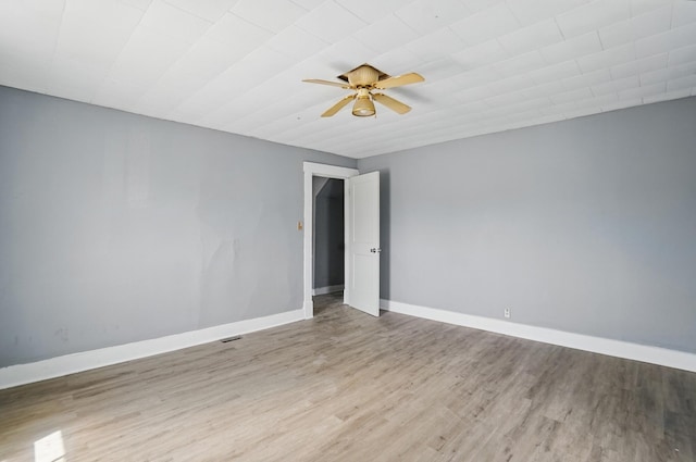 empty room featuring a ceiling fan, visible vents, wood finished floors, and baseboards