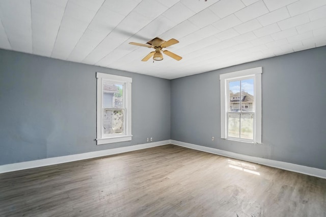 spare room with a wealth of natural light, ceiling fan, wood finished floors, and baseboards