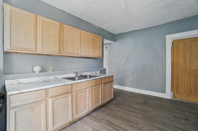 kitchen with a sink, light countertops, baseboards, light brown cabinetry, and dark wood-type flooring