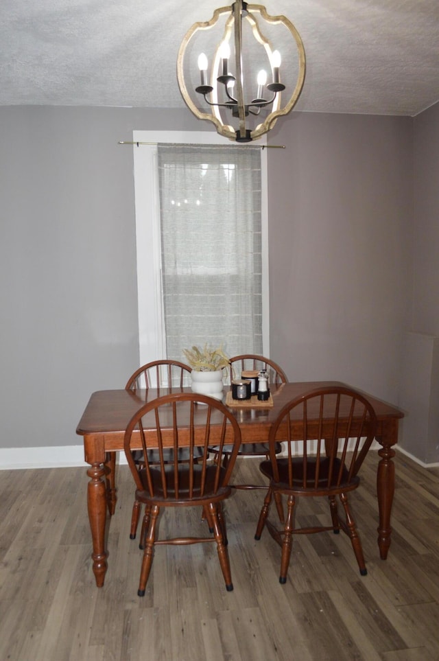 dining space with baseboards, a textured ceiling, an inviting chandelier, and wood finished floors