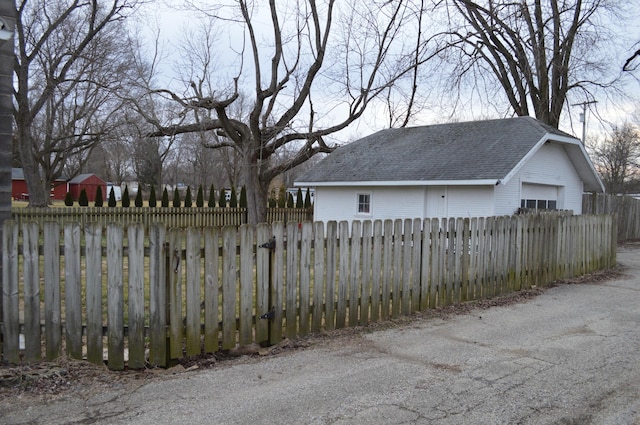 exterior space featuring a fenced front yard, an outdoor structure, a shingled roof, and a garage