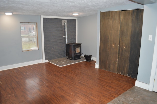 unfurnished living room with a wood stove, a textured ceiling, baseboards, and wood finished floors