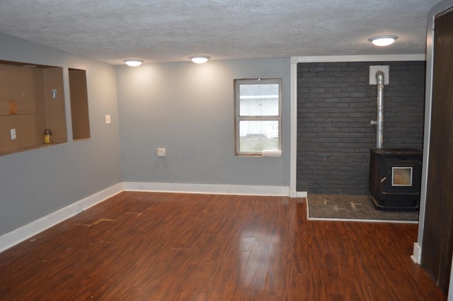 unfurnished living room with a textured ceiling, wood finished floors, a wood stove, and baseboards