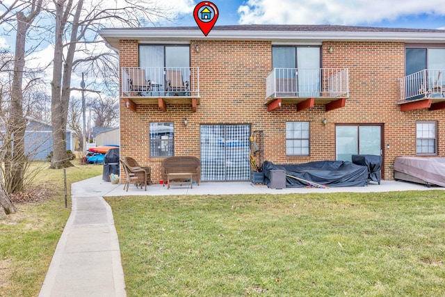 rear view of house with a lawn, brick siding, a patio area, and a balcony