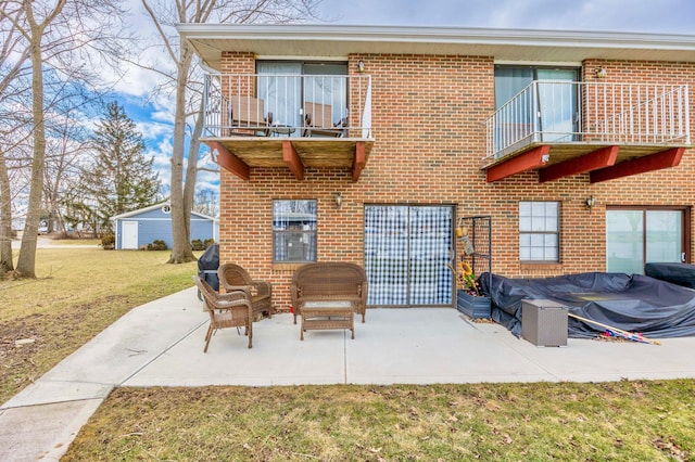 back of house featuring brick siding, a yard, a patio area, and a balcony