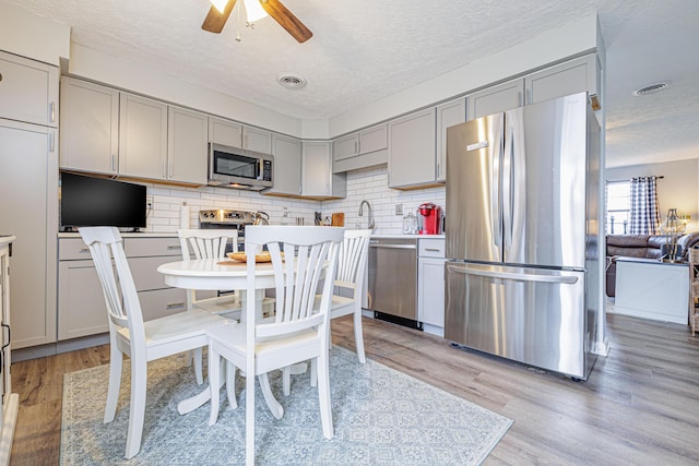 kitchen featuring a textured ceiling, light wood finished floors, gray cabinets, and stainless steel appliances
