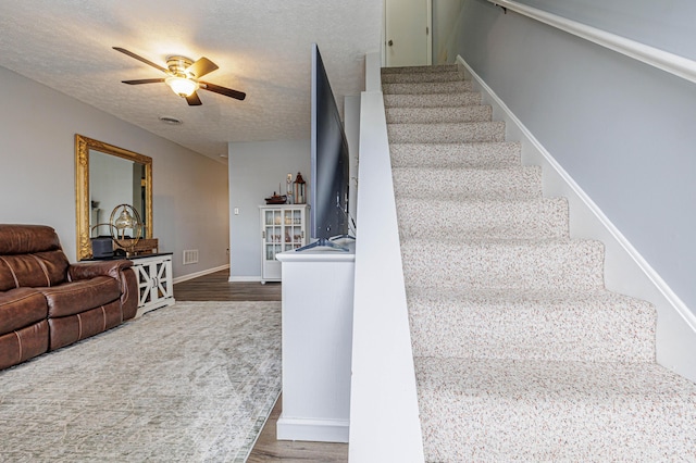 staircase with wood finished floors, a textured ceiling, baseboards, and ceiling fan