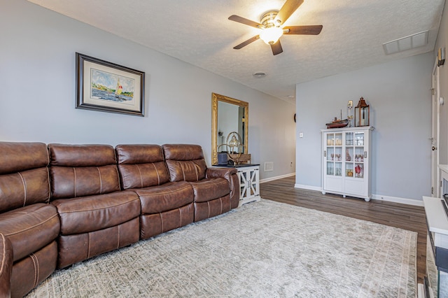 living area featuring a ceiling fan, wood finished floors, visible vents, and a textured ceiling