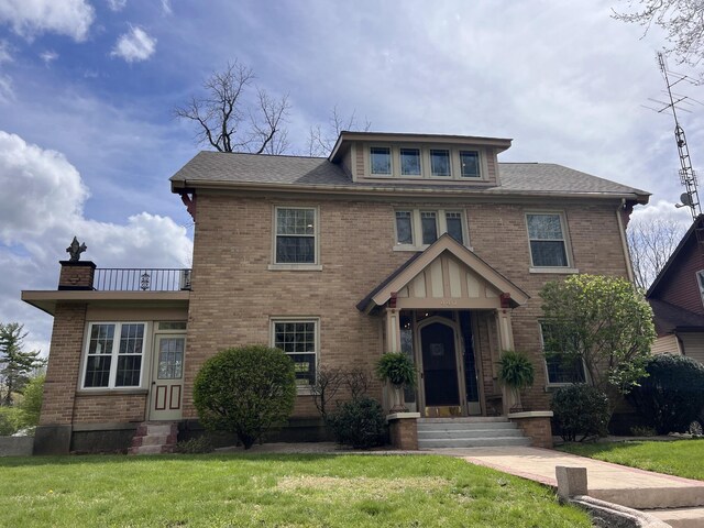 view of front of home with a chimney, brick siding, and a front yard