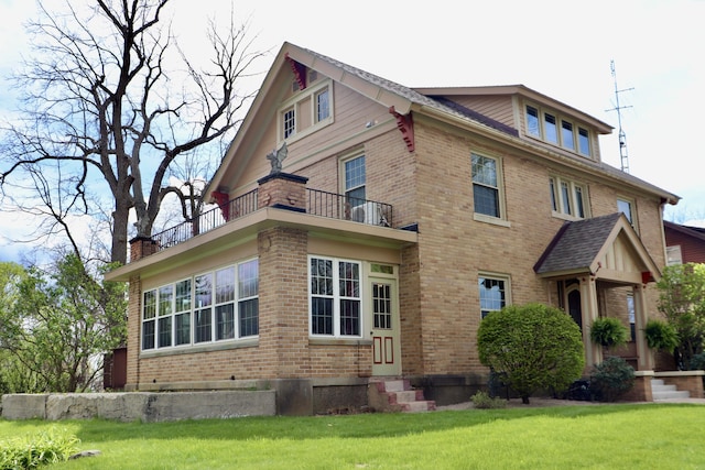 view of front of property featuring brick siding, entry steps, a front yard, and a balcony