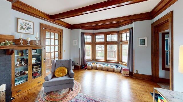 sitting room with beamed ceiling, baseboards, wood finished floors, and ornamental molding
