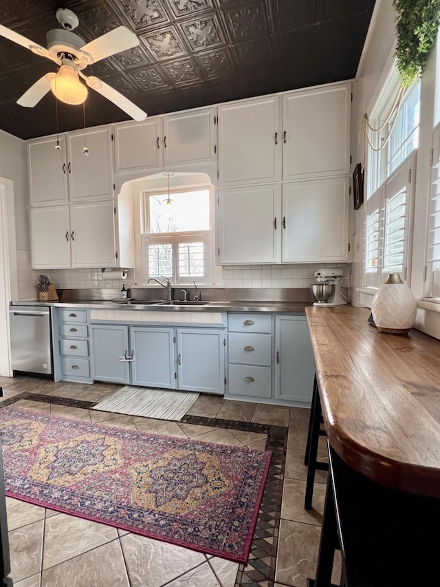 kitchen featuring stainless steel counters, a sink, tasteful backsplash, white cabinetry, and dishwasher