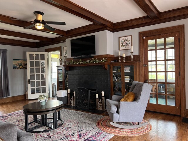 living area with beamed ceiling, wood finished floors, a brick fireplace, and a ceiling fan