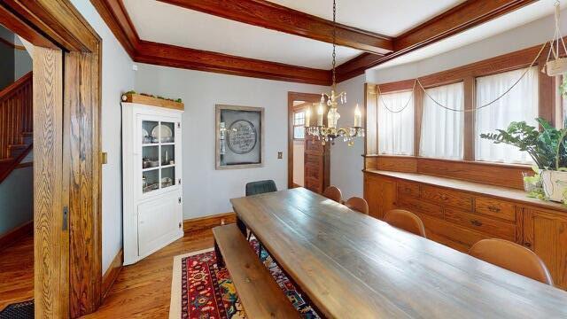 dining room with wood finished floors, beamed ceiling, baseboards, a chandelier, and stairs