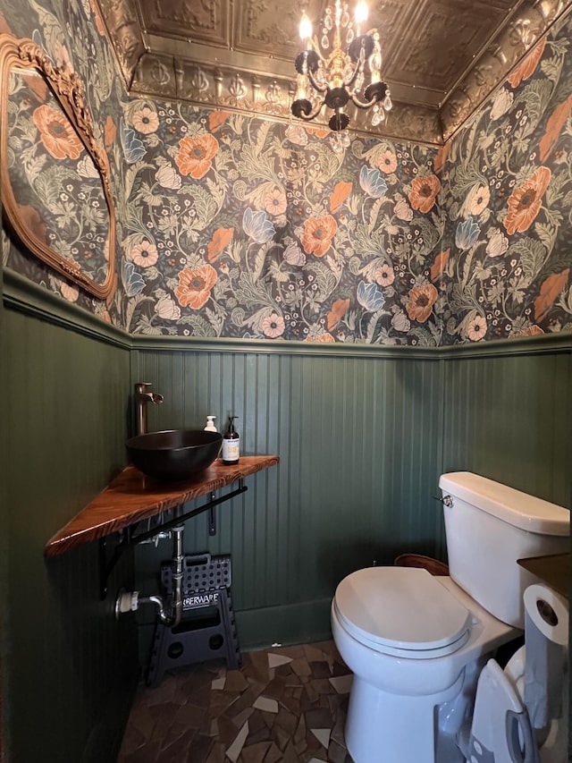 half bathroom with a wainscoted wall, a sink, an ornate ceiling, and toilet