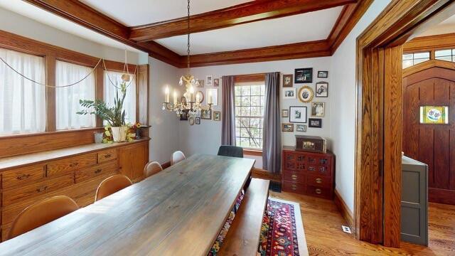 dining area with light wood finished floors, plenty of natural light, beam ceiling, and a notable chandelier