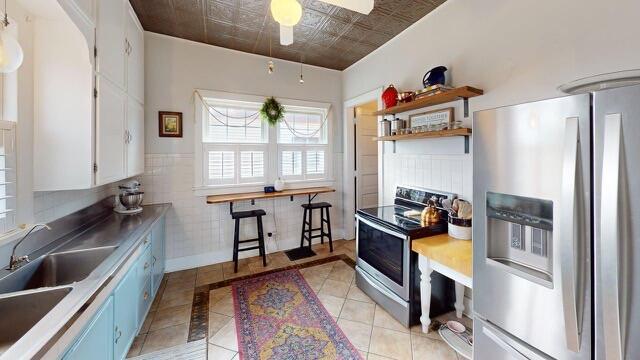 kitchen with blue cabinets, a sink, light tile patterned flooring, an ornate ceiling, and appliances with stainless steel finishes