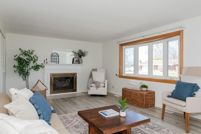 living room with light wood finished floors, a glass covered fireplace, and baseboards