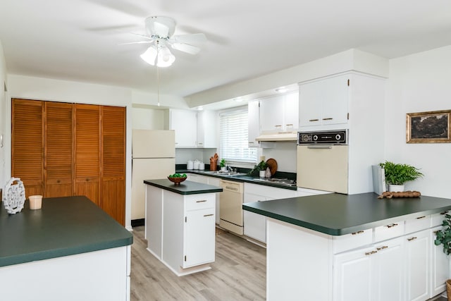 kitchen featuring white appliances, light wood-style floors, under cabinet range hood, dark countertops, and a center island