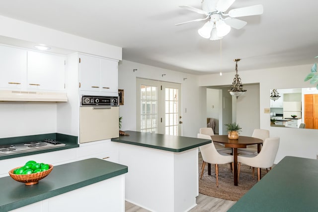 kitchen featuring dark countertops, light wood finished floors, a peninsula, under cabinet range hood, and white oven