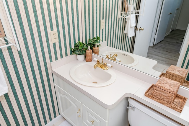 bathroom with toilet, vanity, and wallpapered walls