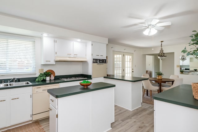 kitchen with a sink, plenty of natural light, dark countertops, a center island, and white appliances