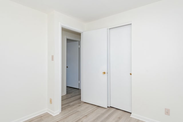 unfurnished bedroom featuring light wood finished floors, a closet, and baseboards