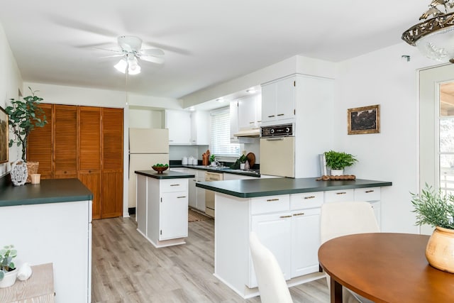 kitchen featuring white appliances, light wood finished floors, a peninsula, under cabinet range hood, and dark countertops