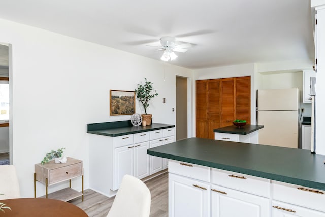 kitchen with light wood finished floors, freestanding refrigerator, ceiling fan, white cabinetry, and dark countertops